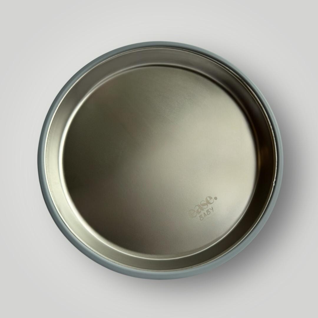 A round stainless steel plate shown from a top-down view on a light gray background. The brand name 'ease.baby is embossed near the bottom right of the interior.