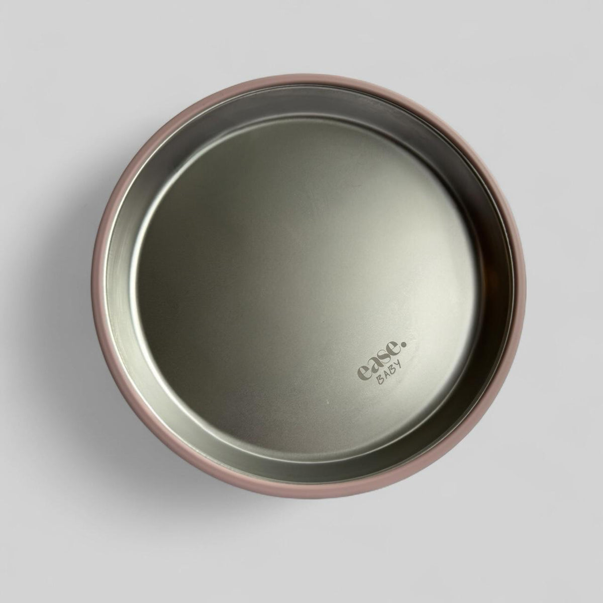 A top-down view of a round stainless steel baby feeding plate with a dusty rose pink rim, featuring the 'ease.baby' logo printed on the bottom right.