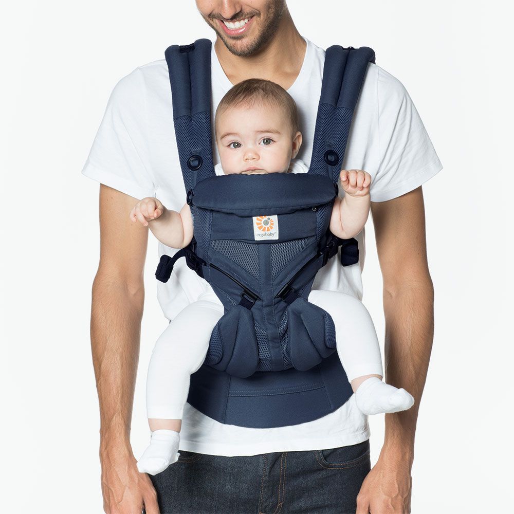 Man holding a baby in a navy blue baby carrier against a white background