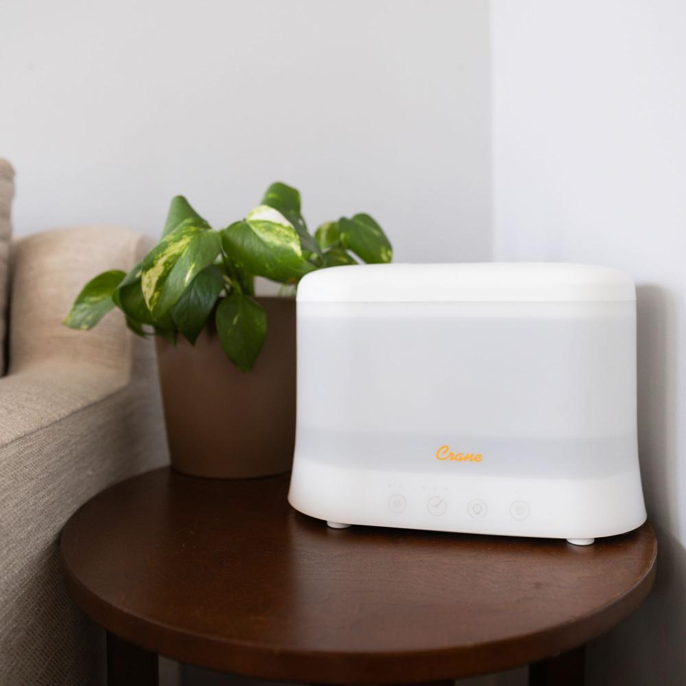 White humidifier on a wooden table next to a potted plant in a room.