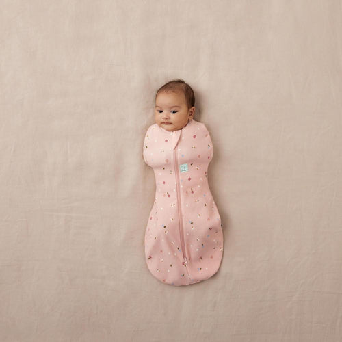 Baby wrapped in a pink sleeping bag with a pattern on a beige surface