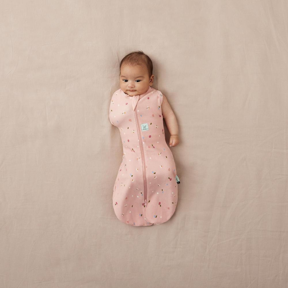 Baby in a pink swaddle bag with one arm out with a pattern on a beige surface