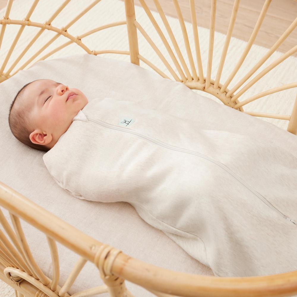 Baby swaddled in a beige coloured zip swaddle bag lying in a wooden crib