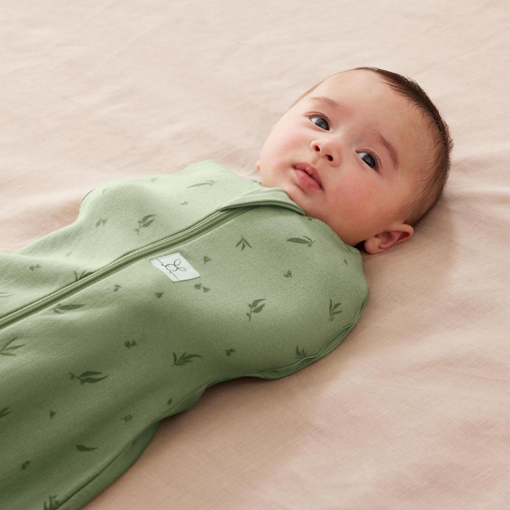 Baby swaddled in a green blanket with a pink background