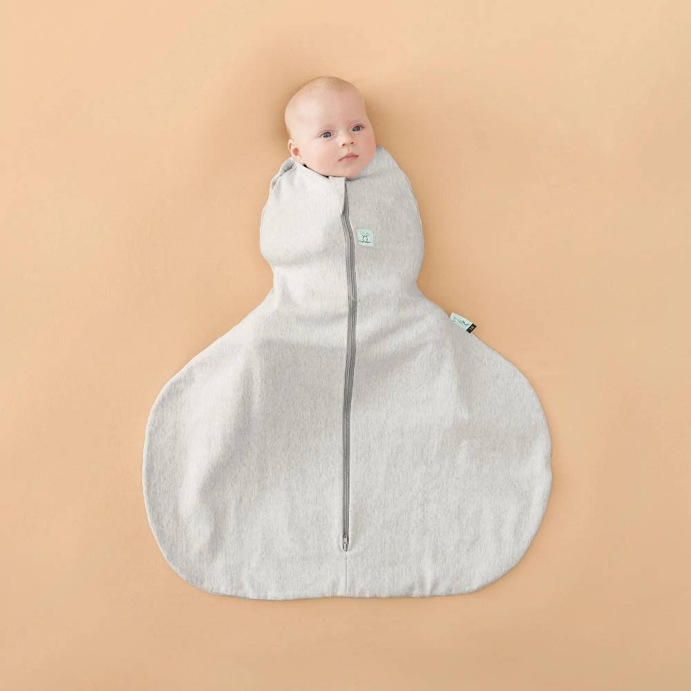 Baby in a grey baby sleeping bag for hip dysplasia with hip brace on a beige blanket