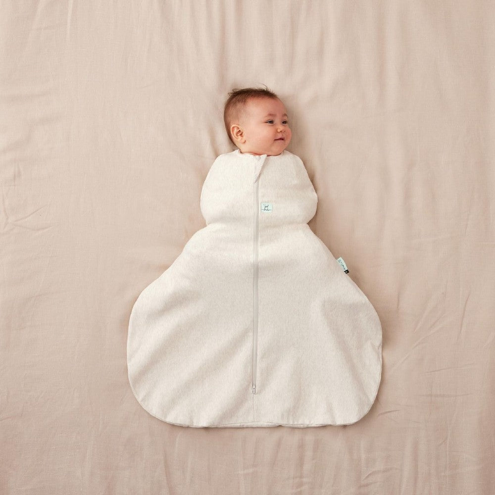 Baby in a beige baby sleeping bag for hip dysplasia with hip[ brace on a beige blanket