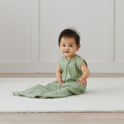 Baby in a green outfit sitting on a white mat with a white wall background