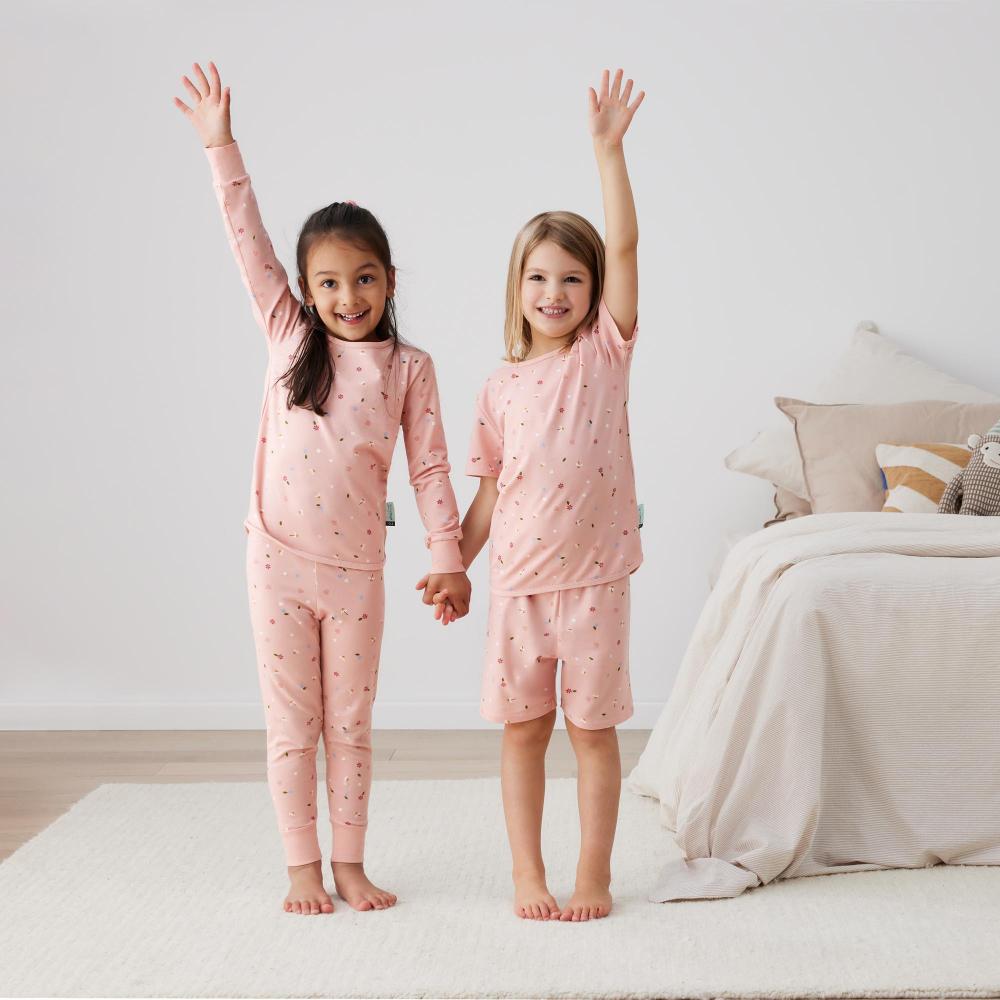 Two children in matching pink pajamas standing in a bedroom.