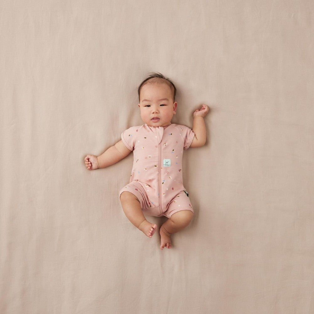 Baby lying on a beige surface wearing a pink onesie with a small logo.
