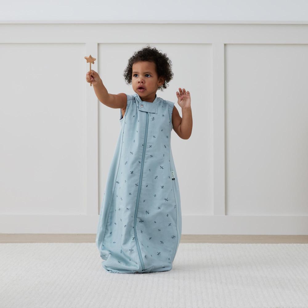 Child in a light blue sleeveless sleeping bag with a star wand, standing on a white surface.