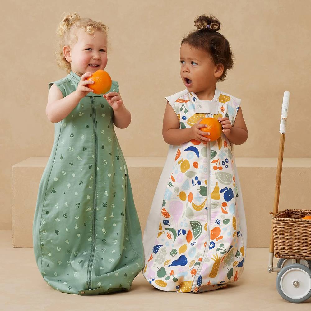 Two children in patterned sleep sacks holding oranges on a beige background