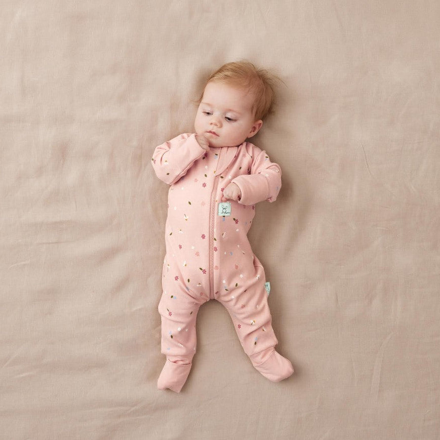 Baby in a pink onesie lying on a beige blanket