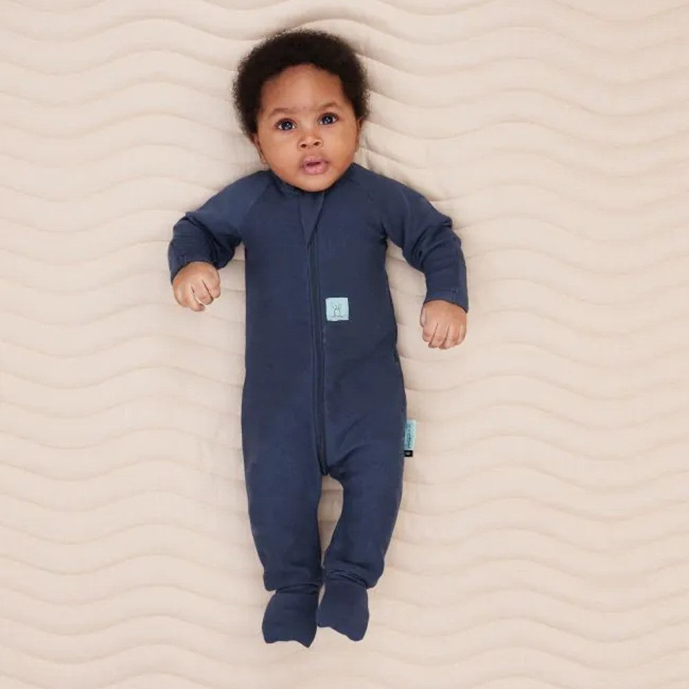 Baby wearing a navy blue onesie lying on a beige textured surface