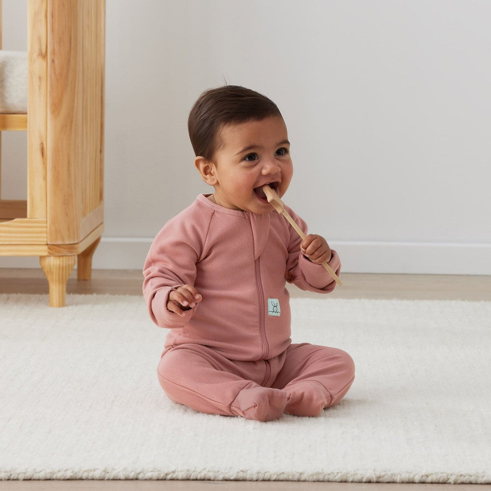 Baby in pink outfit sitting on a white rug indoors