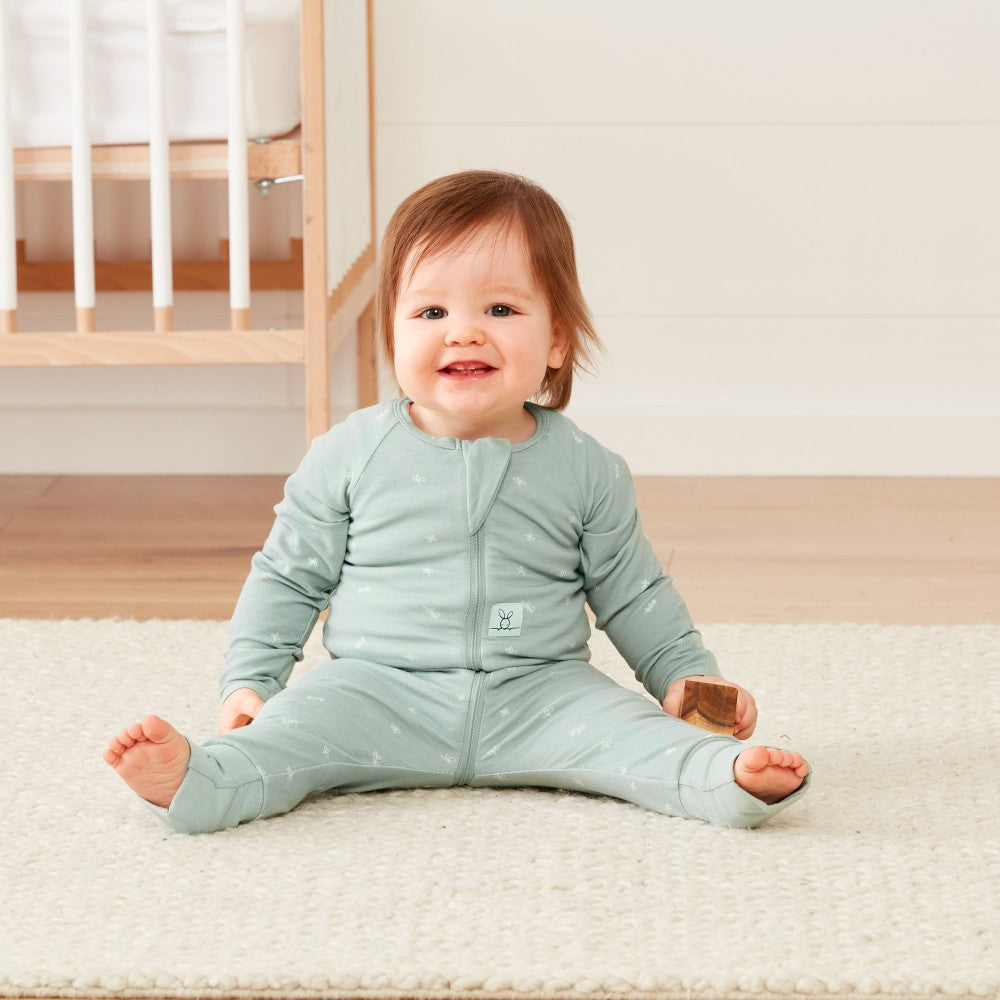 Baby wearing a light blue onesie sitting on a white rug.