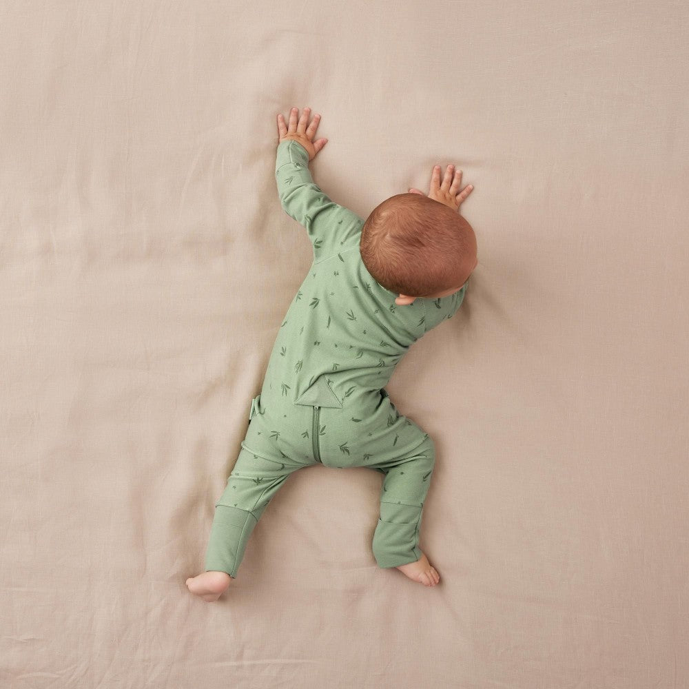 Baby in a green onesie lying on a beige blanket