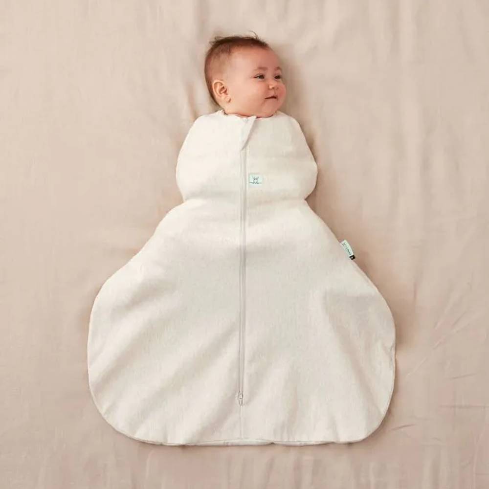 Baby in a beige hip dysplasia baby sleeping bag on a beige blanket