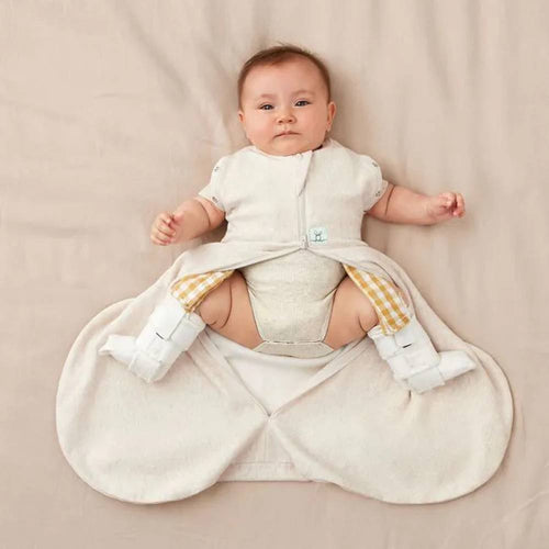 Baby in a beige hip dysplasia baby sleeping bag with hip brace on in a beige blanket