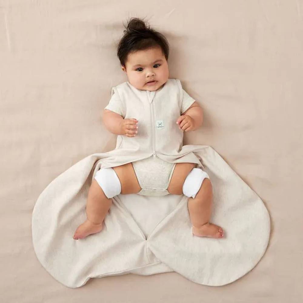Baby lying on a beige blanket wearing a Beige hip dysplasia baby sleeping bag with a hip brace on