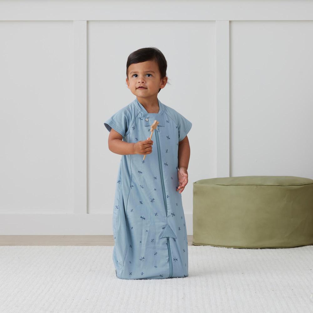 Child wearing a light blue baby sleepsuit with a white wall and green ottoman in the background