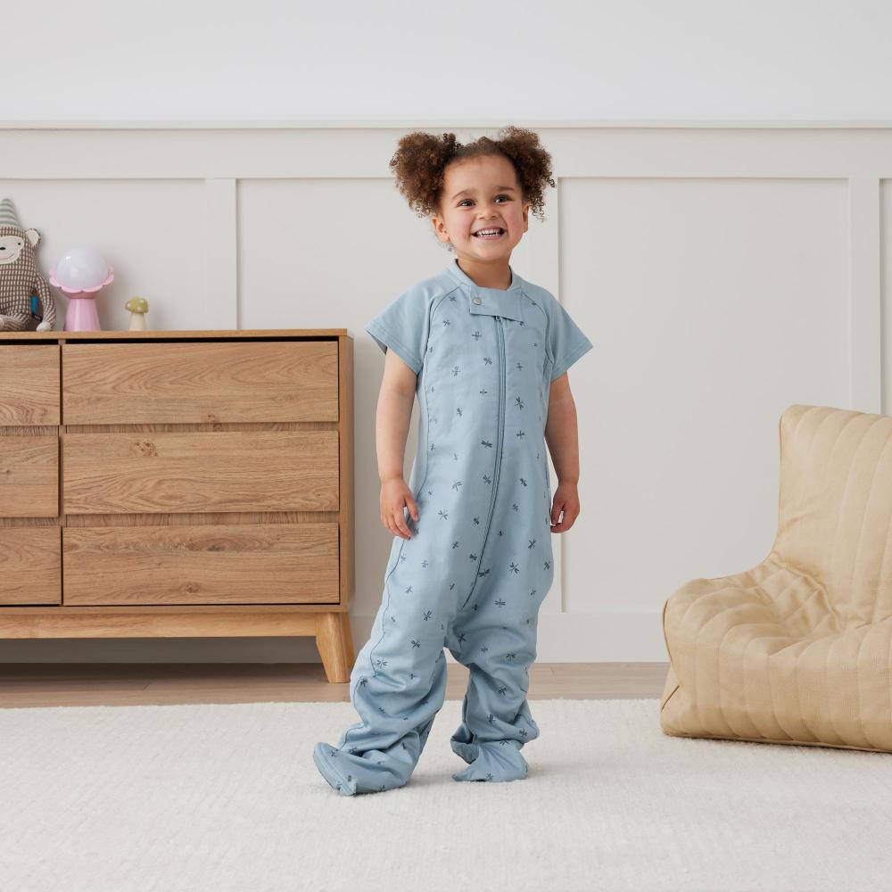 Child wearing a blue onesie in a room with wooden furniture and a beige chair.