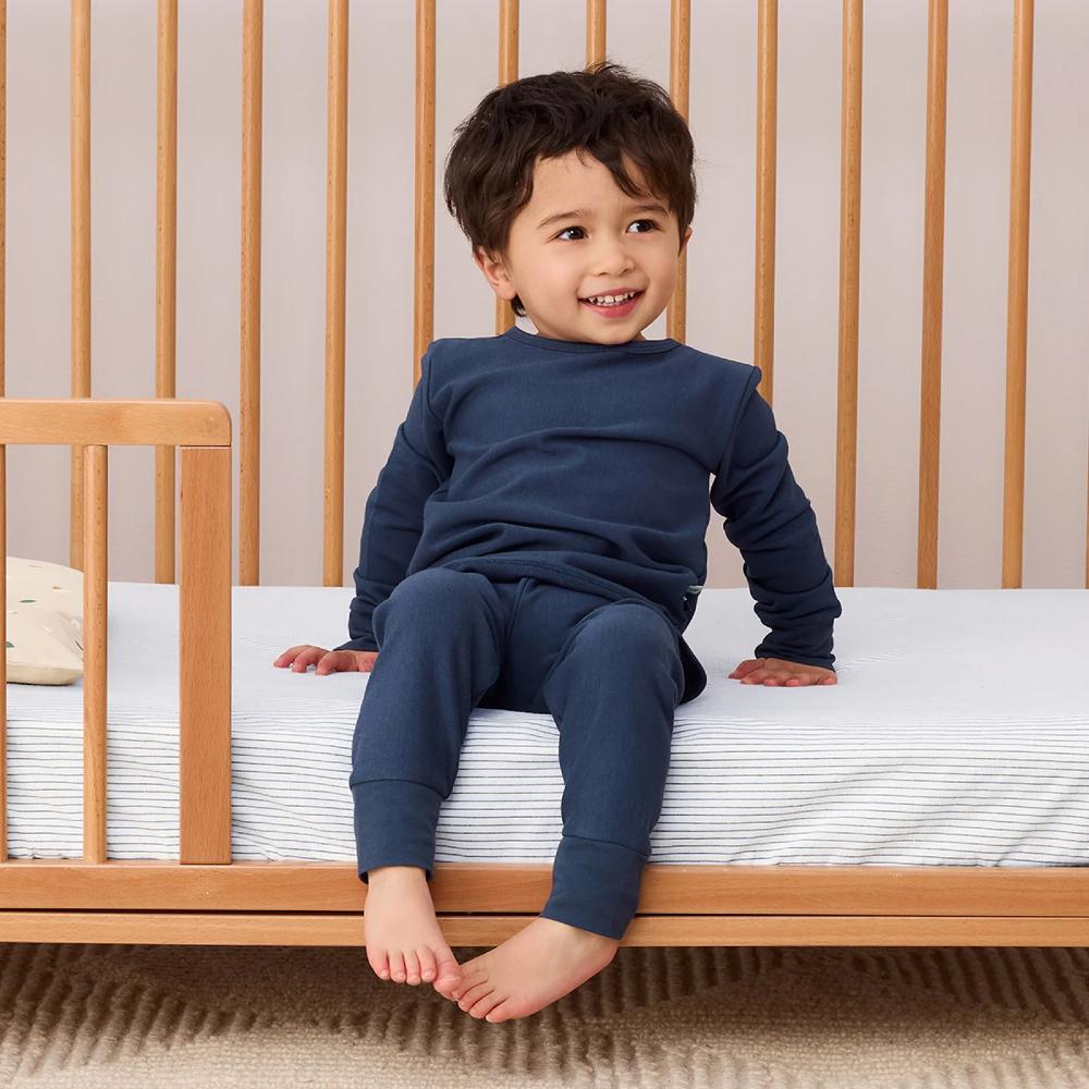 Child sitting on a crib wearing blue pajamas, smiling.