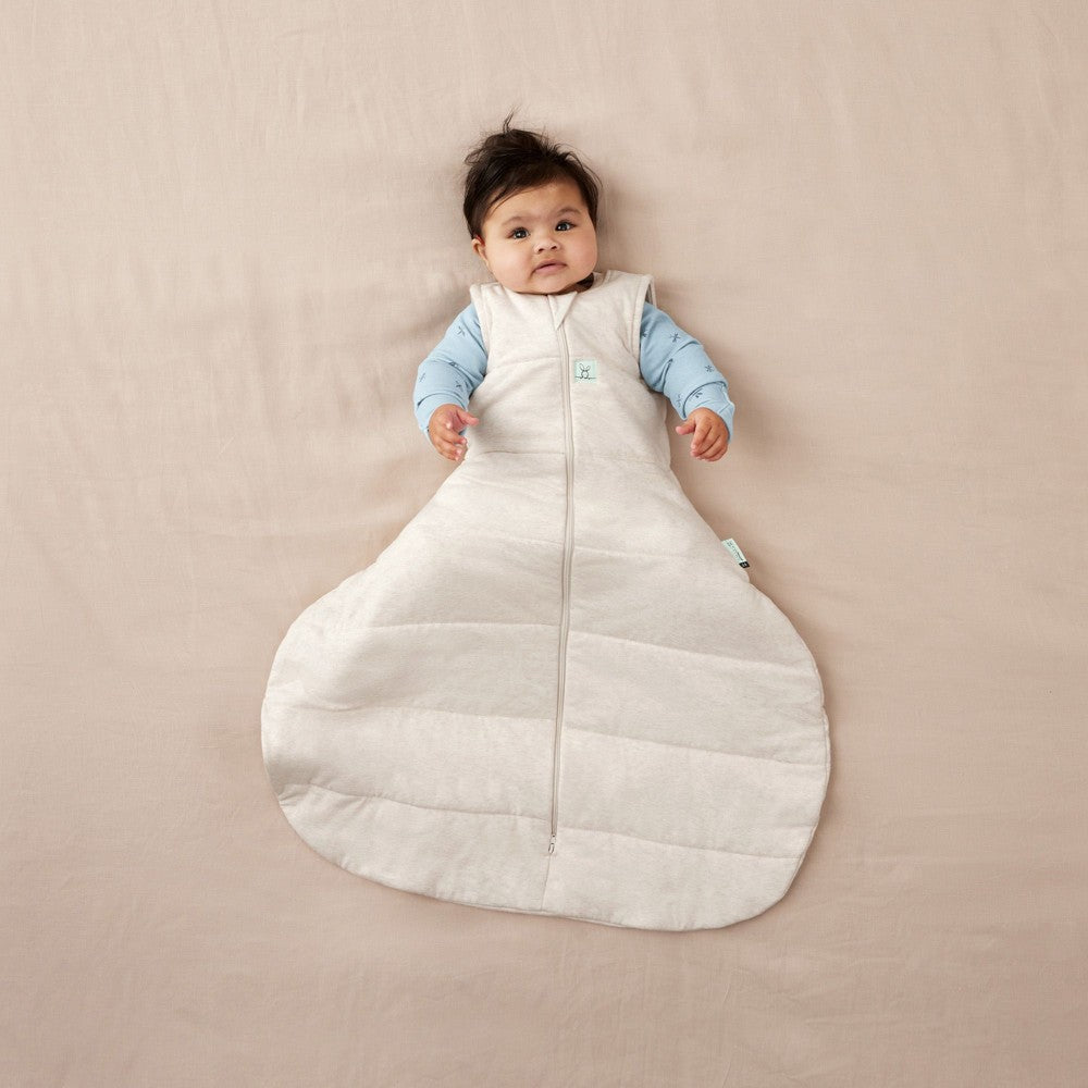 Baby lying on a beige surface wearing a white sleeping bag