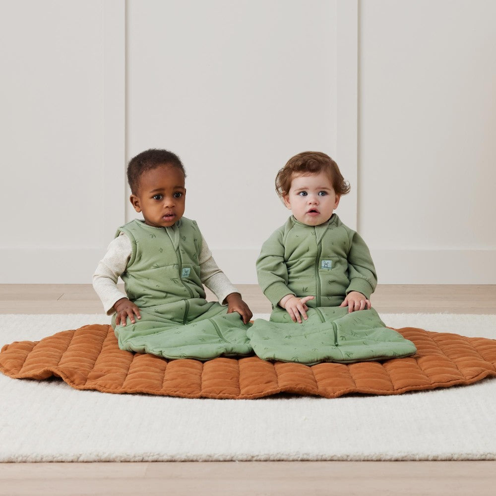 Two children wearing green outfits sitting on a brown quilted blanket.