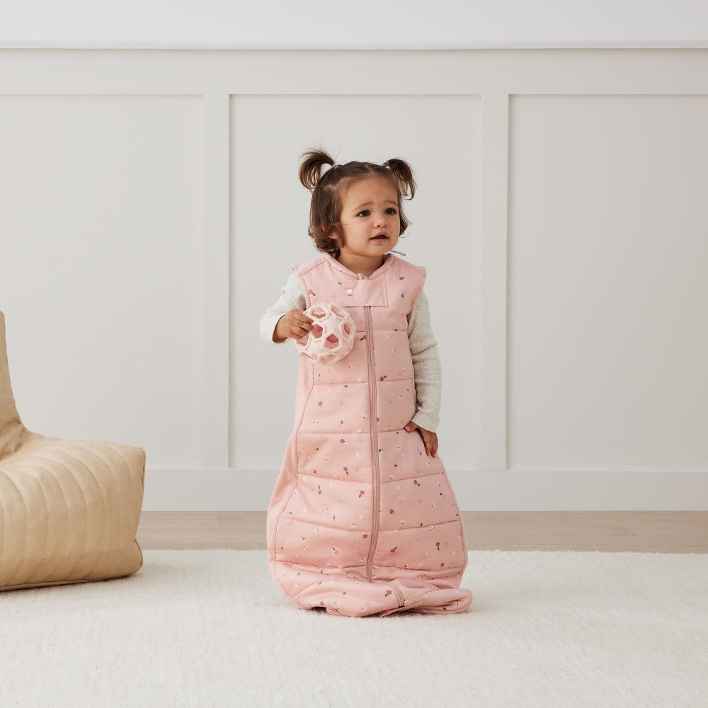 Child wearing a pink quilted sleeping bag in a minimalistic room.