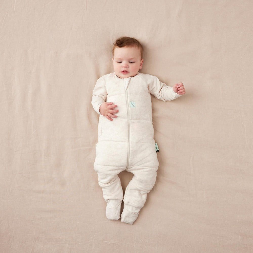 Baby wearing a white quilted onesie lying on a beige surface