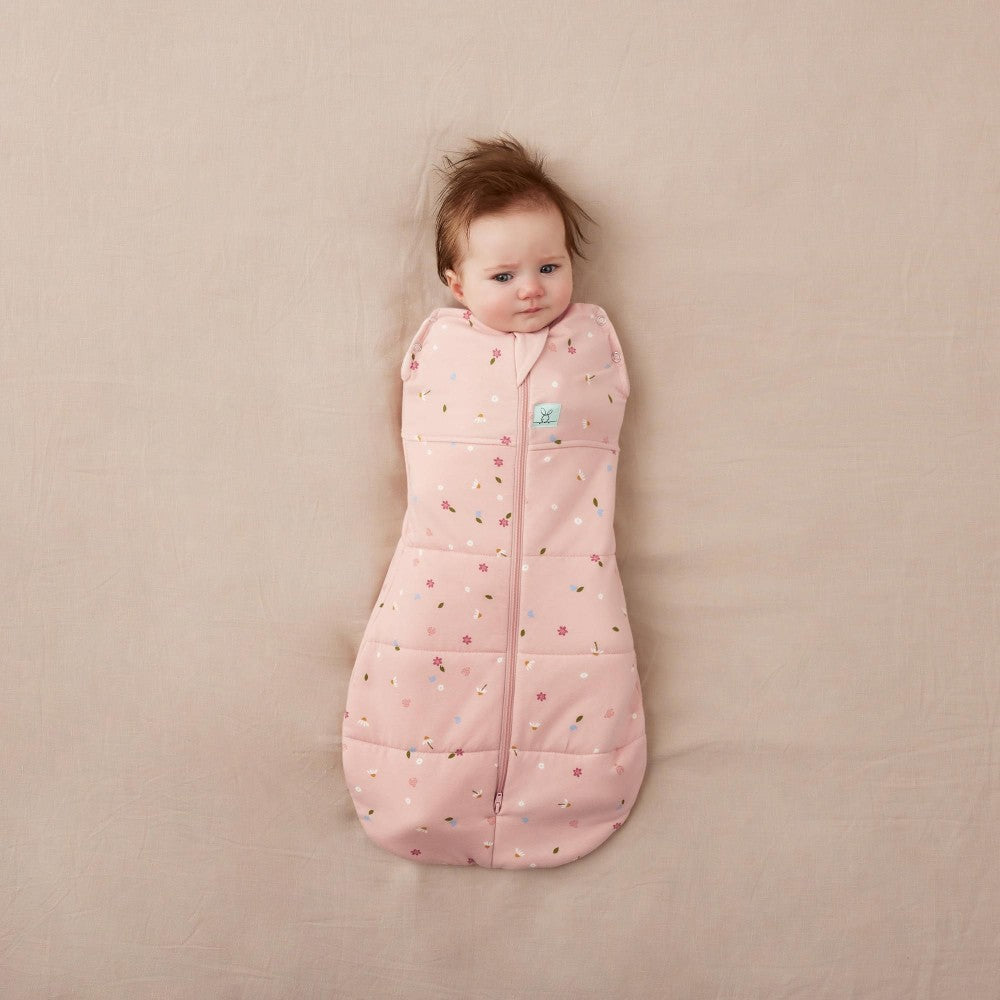 Baby wrapped in a pink patterned quilted winter sleeping bag on a beige surface