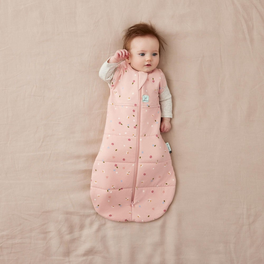 Baby lying on a pink swaddle wrap wearing a pink sleeping bag with a pattern.