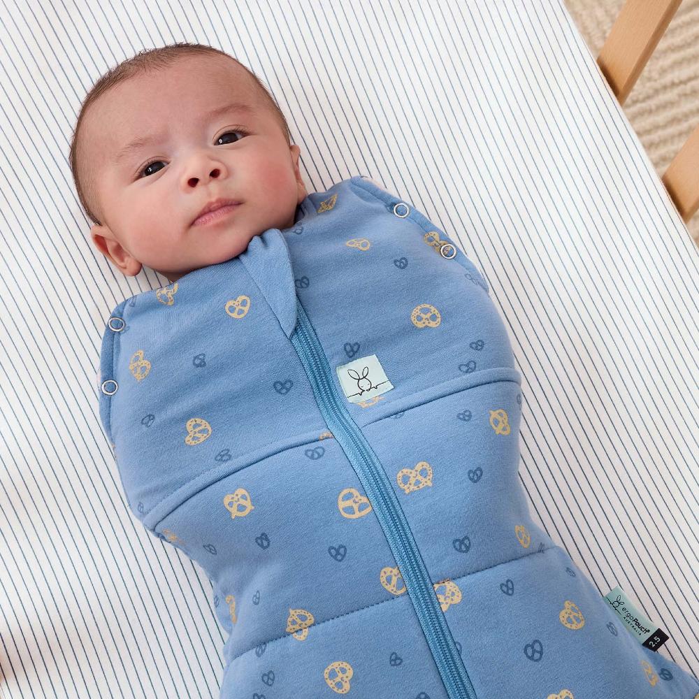 Baby wrapped in a blue swaddle with a pattern, lying on a striped surface.