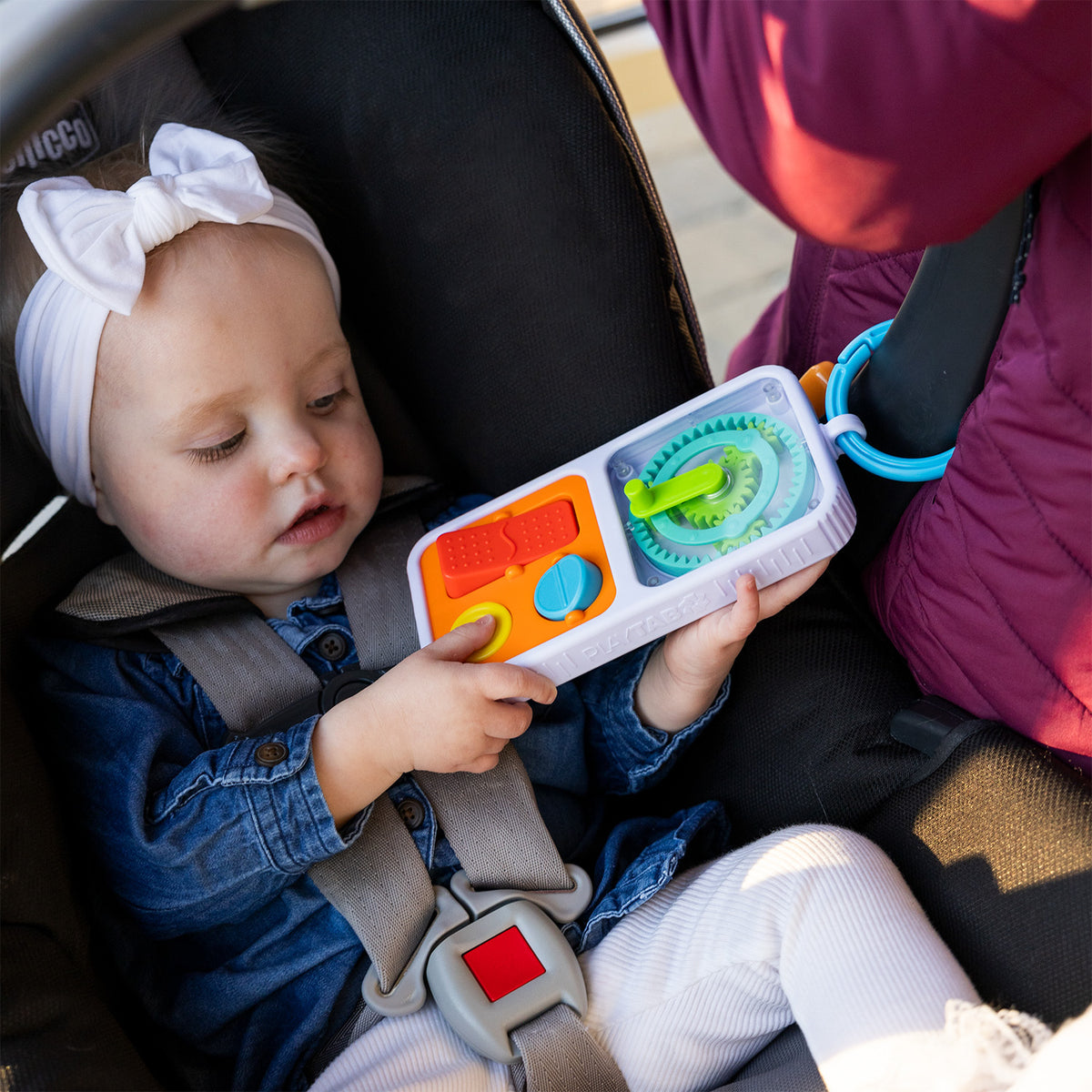 A young child playing with PlayTab Go that is connected to a carseat handle. 