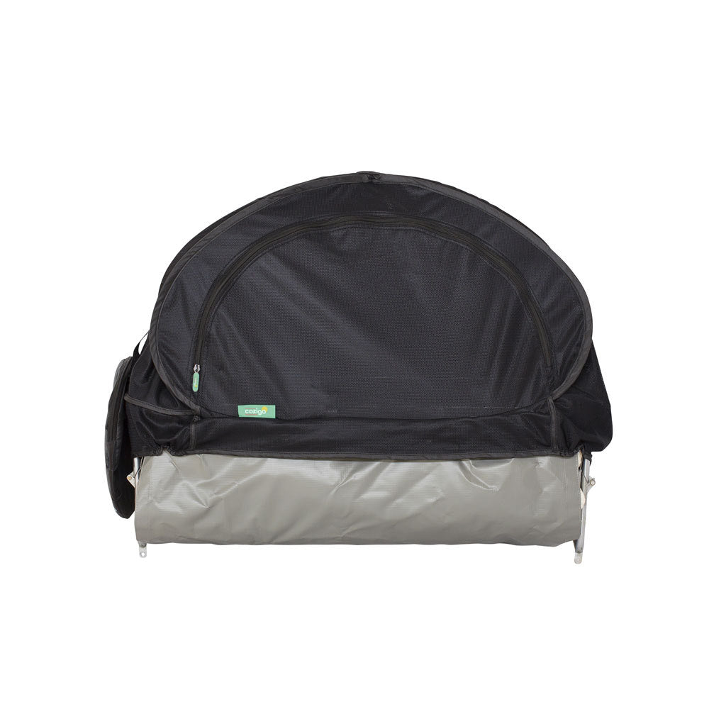 A baby stroller cover with an attached canopy on an airline bassinet. The canopy is black with a small green zipper pull and a tiny green brand tag.