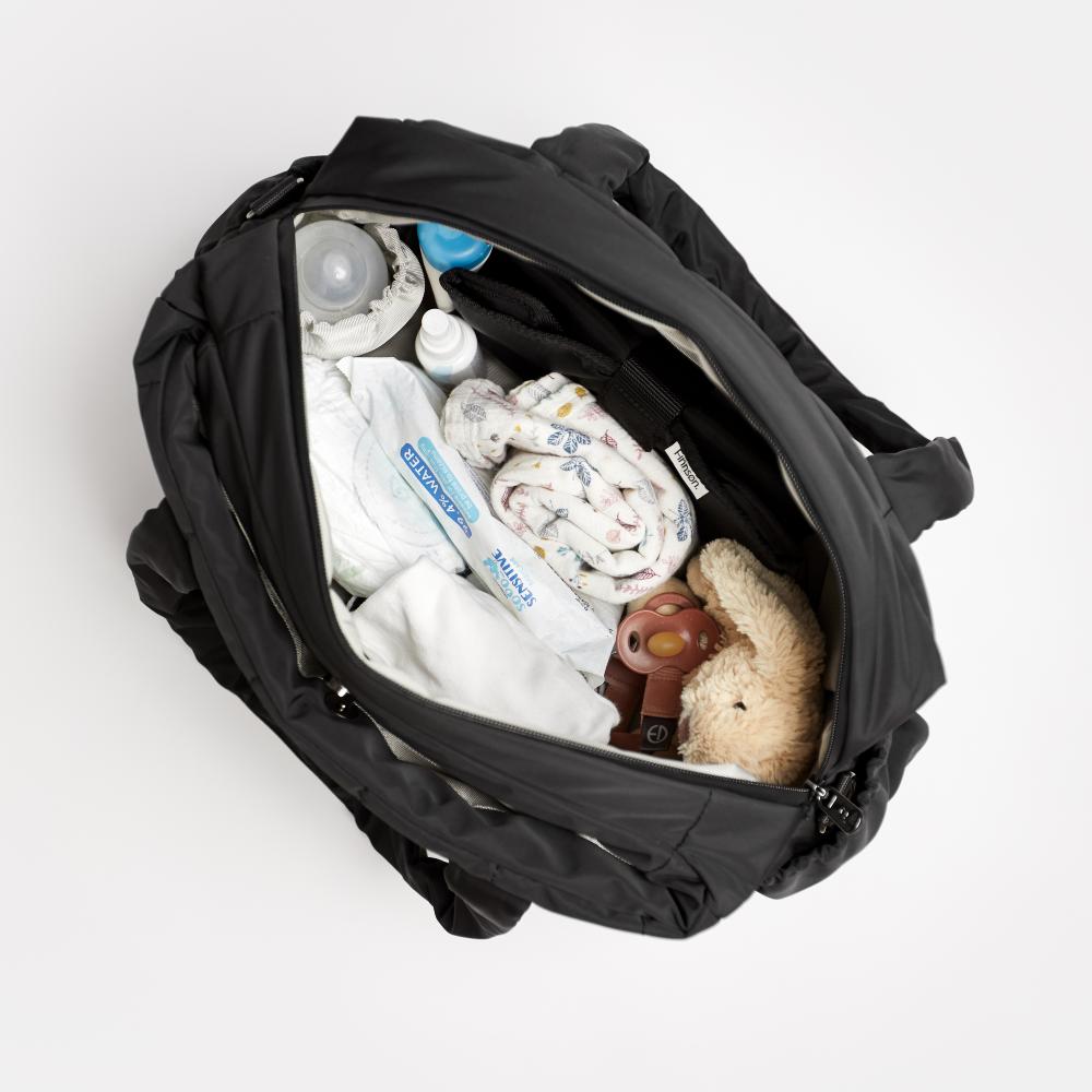 Black Finnson fashion nappy bag open to reveal baby items including a blanket, bottle, and toy on a white background