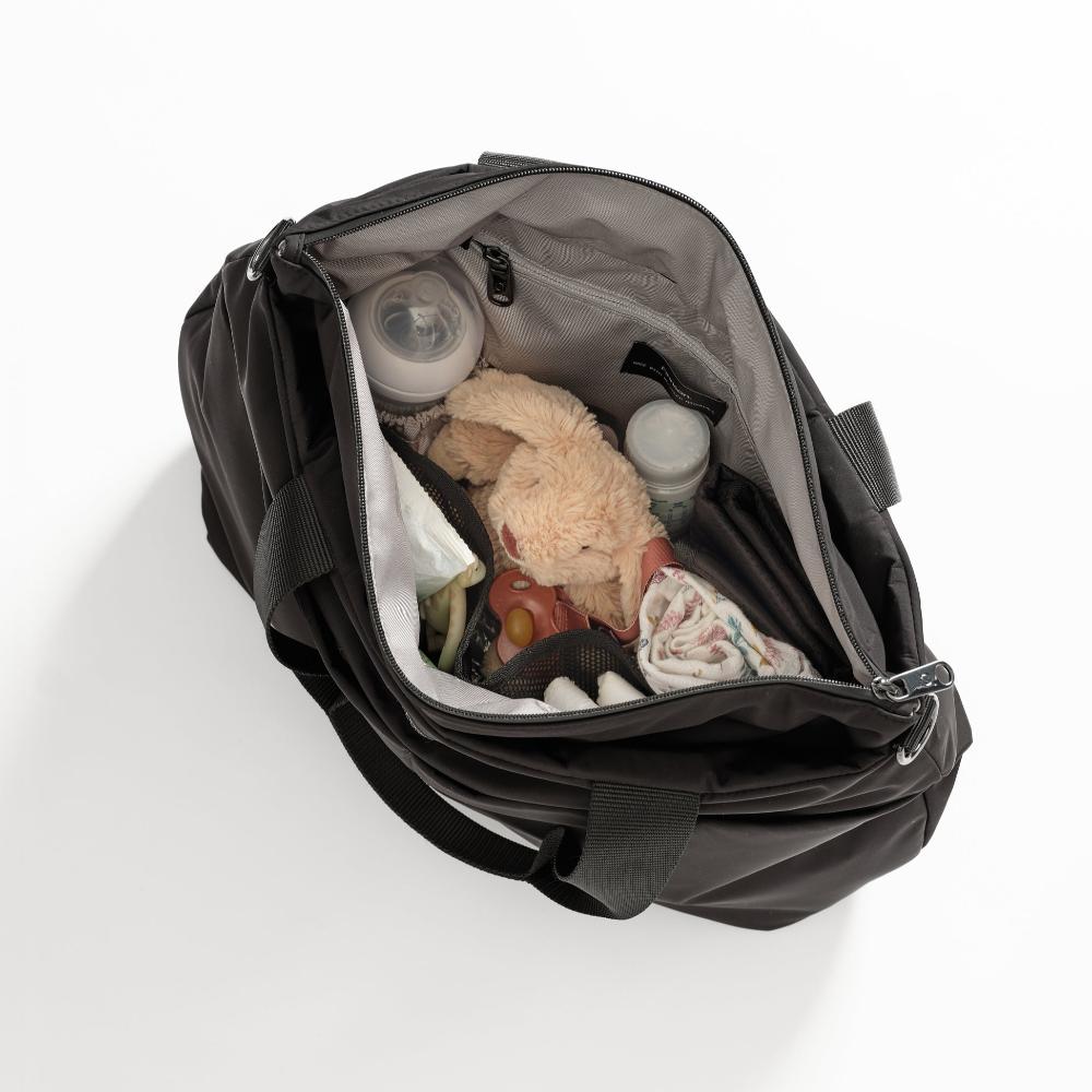 Fashionable black Finnson nappy tote with baby items including a teddy bear, bottles, and clothes on a white background