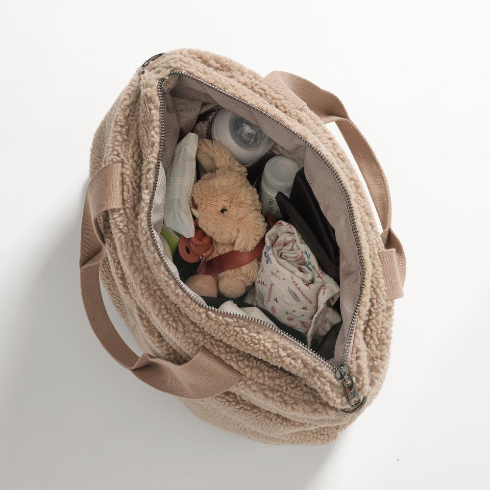 Beige bag with a teddy bear and other items on a white background