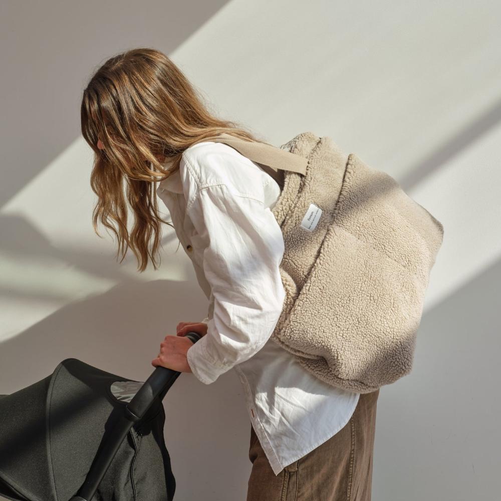 Person wearing a beige fleece backpack with a white wall background