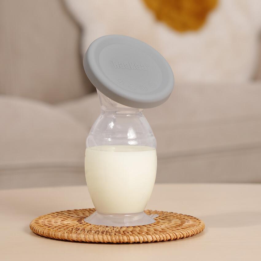 Haakaa  manual breast pump Bottle with milk on a woven coaster against a neutral background