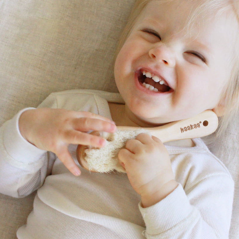 Baby holding goats wool hairbrush and laughing against a soft background