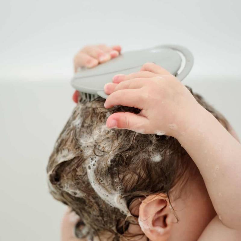 Baby using silicone shampoo brush with soapy hair 