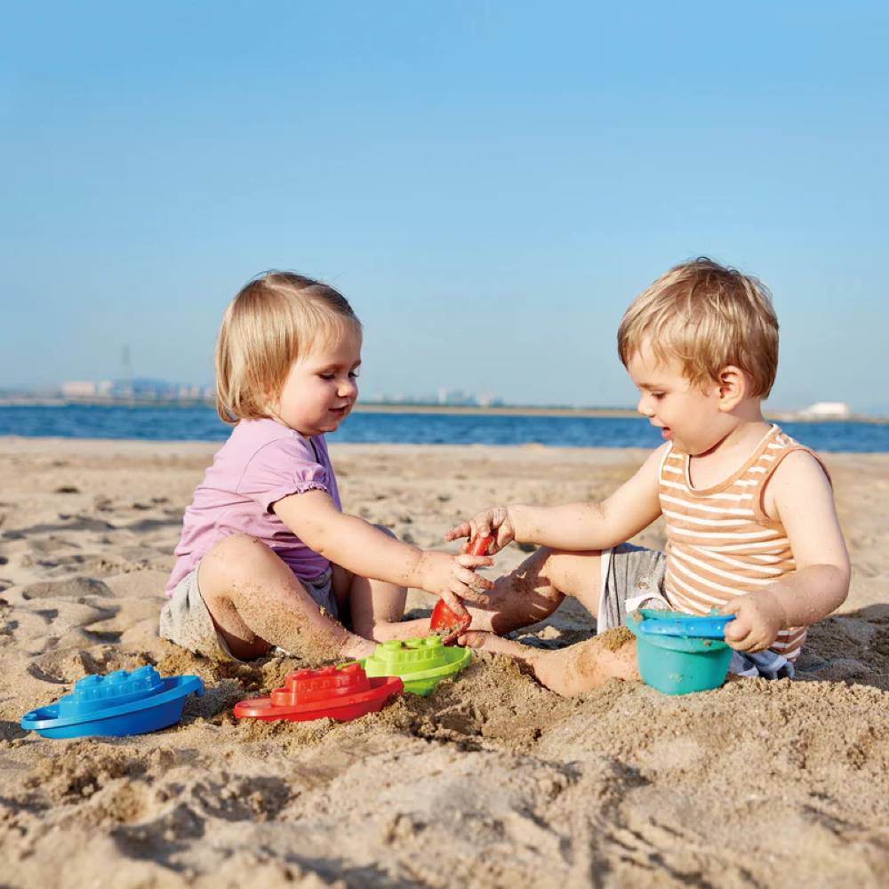 Kids playing with Hape happy boats in sand against ocean view.