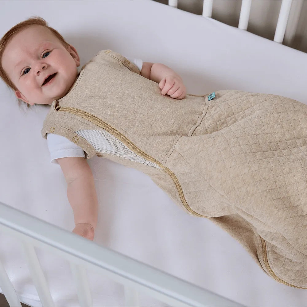Baby lying in a crib wearing a beige sleeping bag
