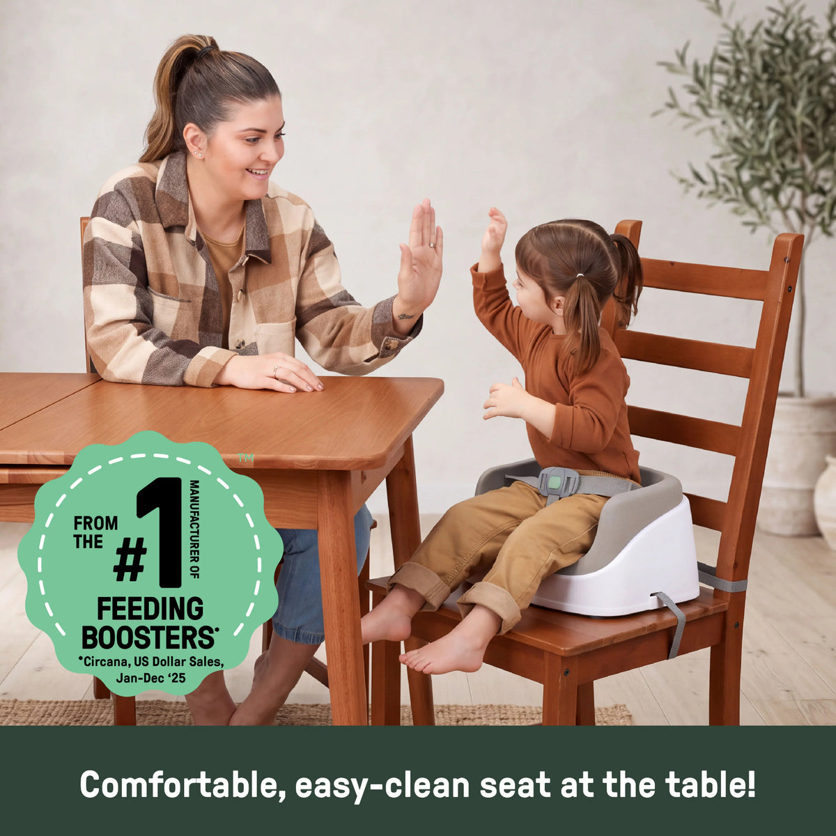 A young child sitting on a booster seat attached to a dining chair, high five-ing a woman. 