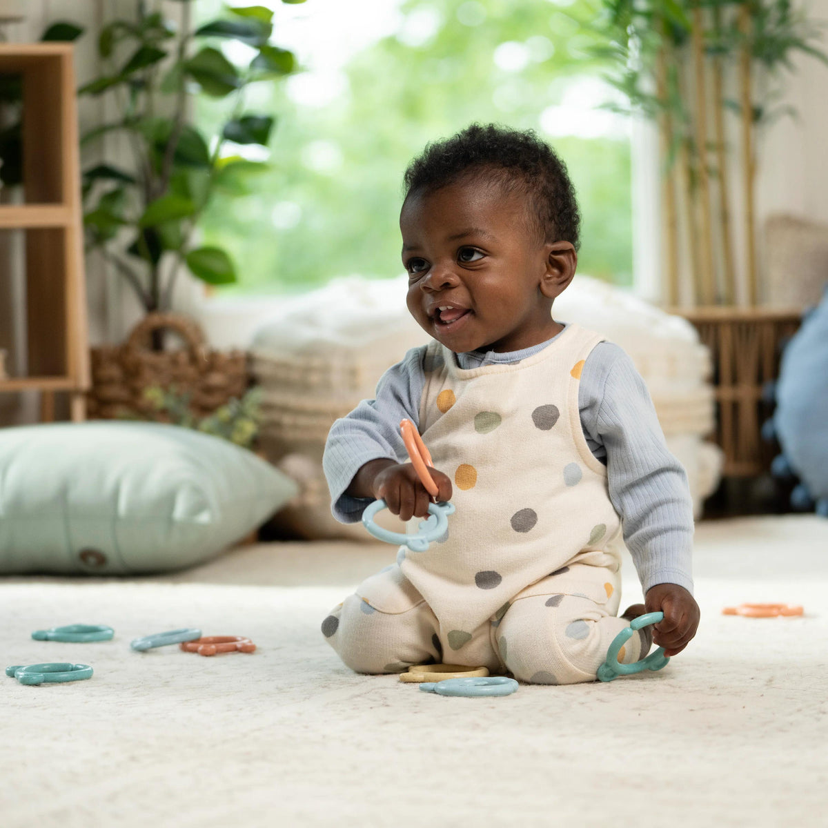 Baby playing with toys on a light-colored floor with plants in the background