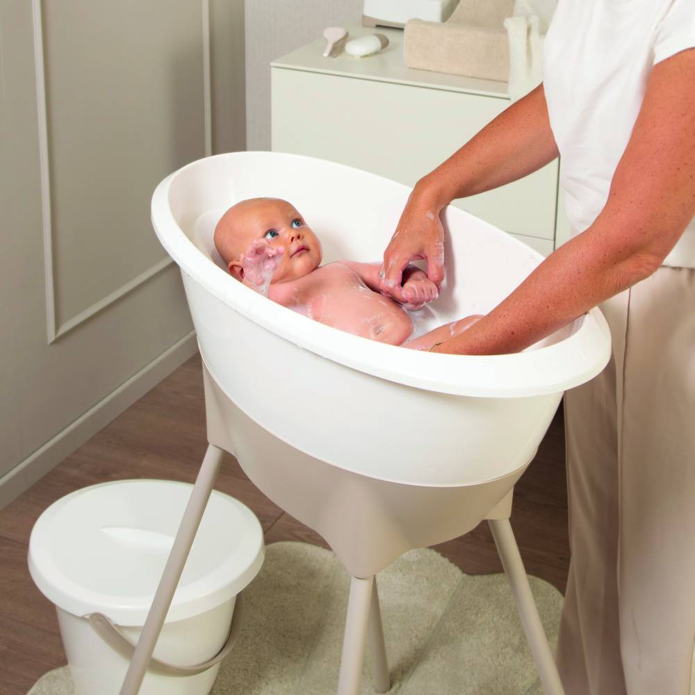 Baby inside a baby bath, on a bath stand. 