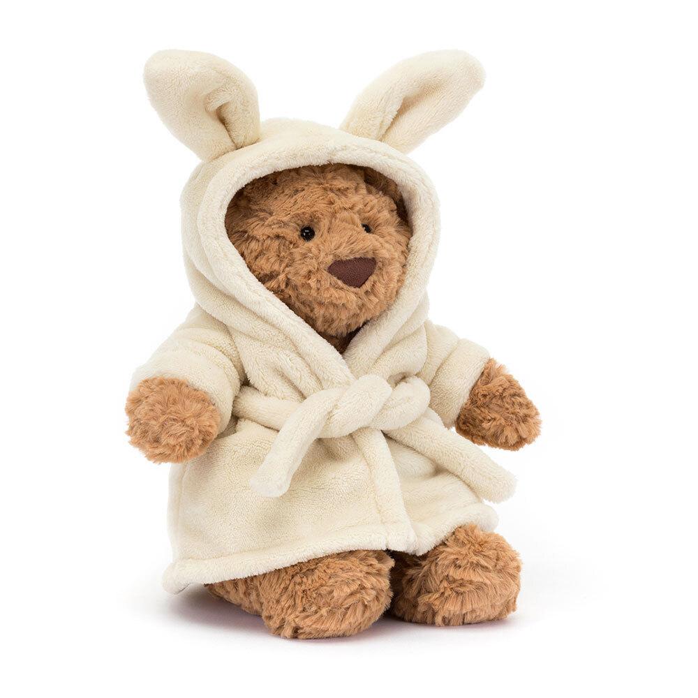 Brown Jellycat soft toy bear with cream robe against white background.