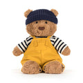 Brown Jellycat bear soft toy with yellow and striped outfit with blue hat against white background.