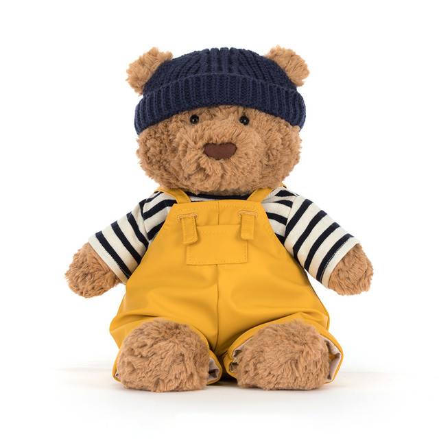 Brown Jellycat bear soft toy with yellow and striped outfit with blue hat against white background.